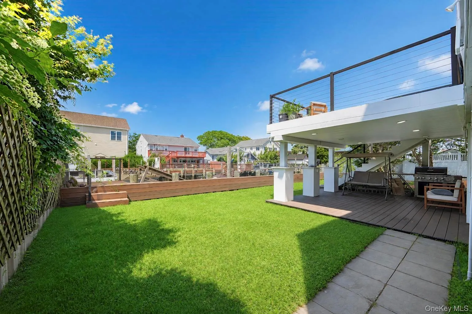 Expansive green lawn with a lower wood-finish deck and an upper deck featuring cable railings Expansive green lawn with a lower wood-finish deck and an upper deck featuring cable railings