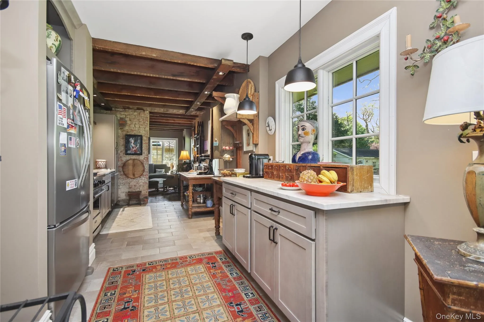 Exposed wood beam ceiling, stainless steel range with overhead vent hood, cabinetry with dark hardware, and light-colored flooring Exposed wood beam ceiling, stainless steel range with overhead vent hood, cabinetry with dark hardware, and light-colored flooring