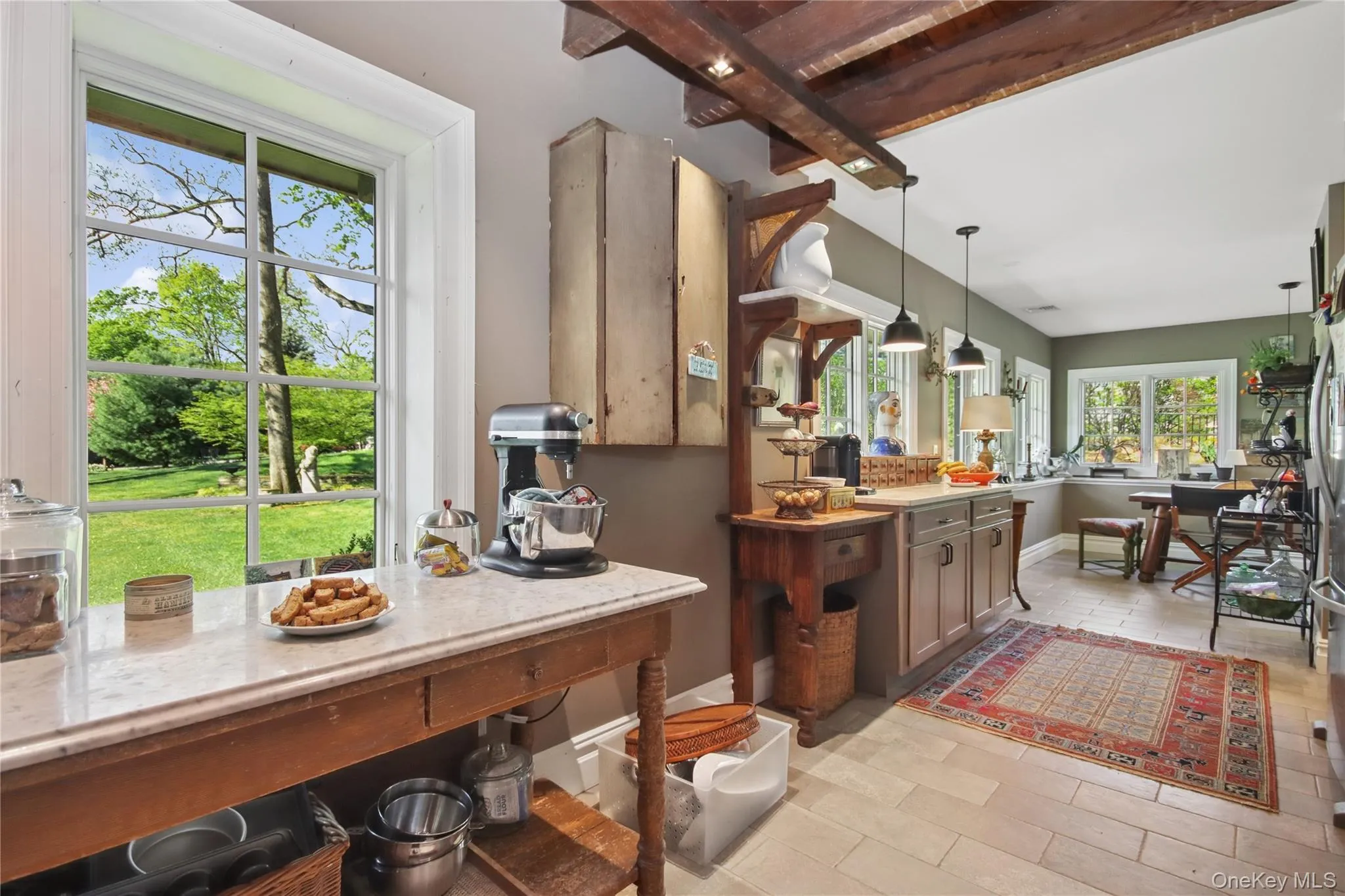 Exposed wood beam ceiling, stainless steel range with overhead vent hood, cabinetry with dark hardware, and light-colored flooring Exposed wood beam ceiling, stainless steel range with overhead vent hood, cabinetry with dark hardware, and light-colored flooring