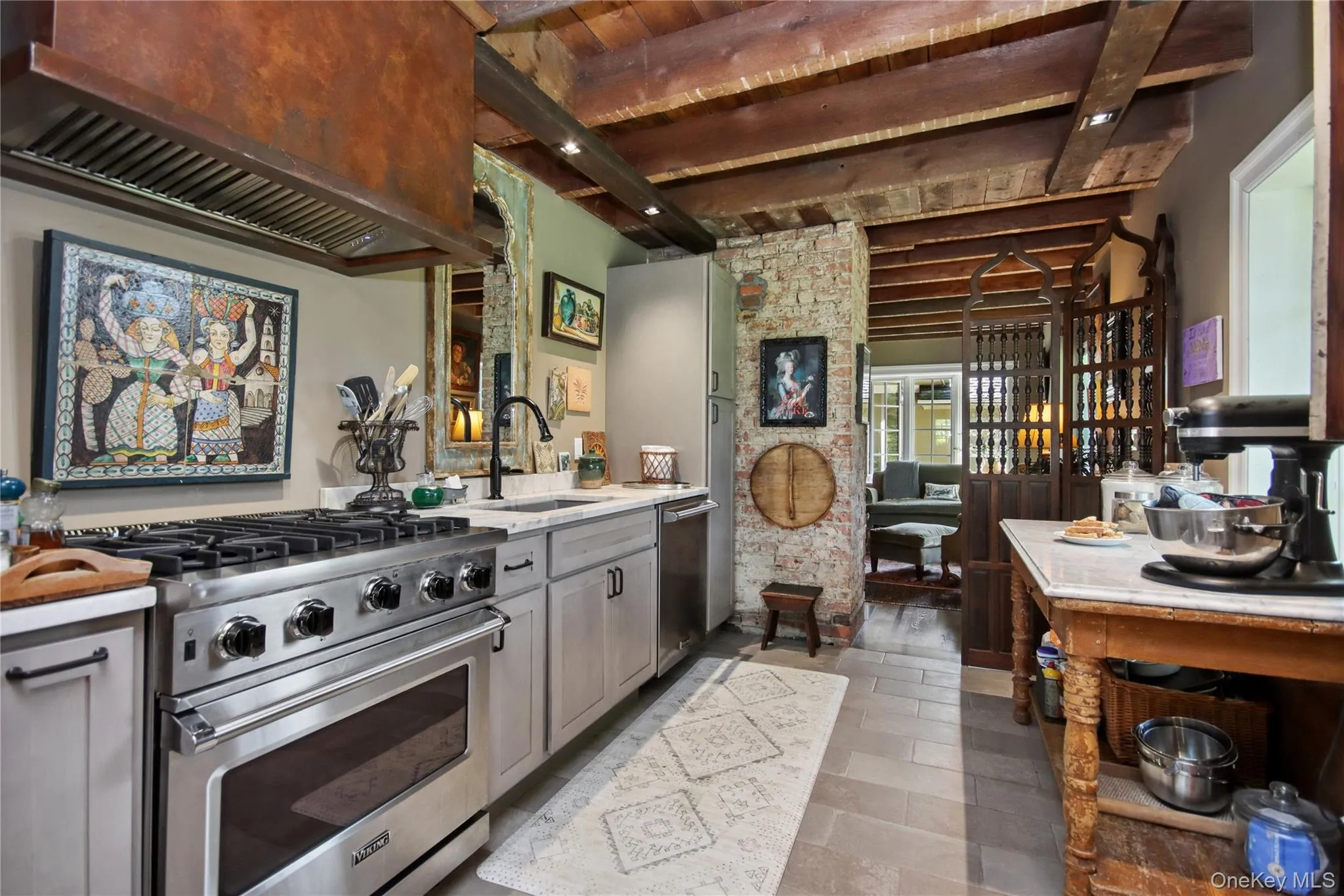 Exposed wood beam ceiling, stainless steel range with overhead vent hood, cabinetry with dark hardware, and light-colored flooring Exposed wood beam ceiling, stainless steel range with overhead vent hood, cabinetry with dark hardware, and light-colored flooring