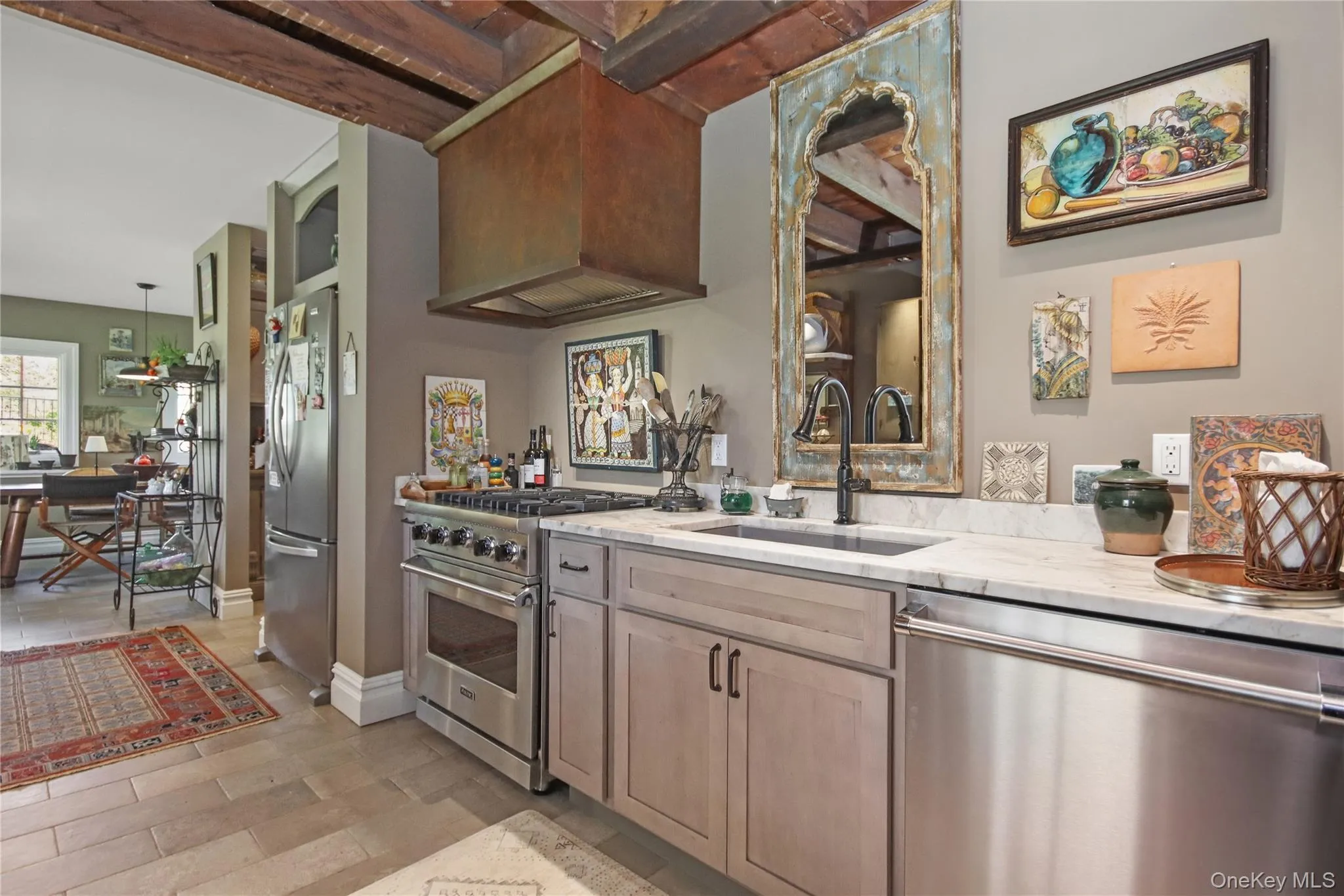 Exposed wood beam ceiling, stainless steel range with overhead vent hood, cabinetry with dark hardware, and light-colored flooring Exposed wood beam ceiling, stainless steel range with overhead vent hood, cabinetry with dark hardware, and light-colored flooring