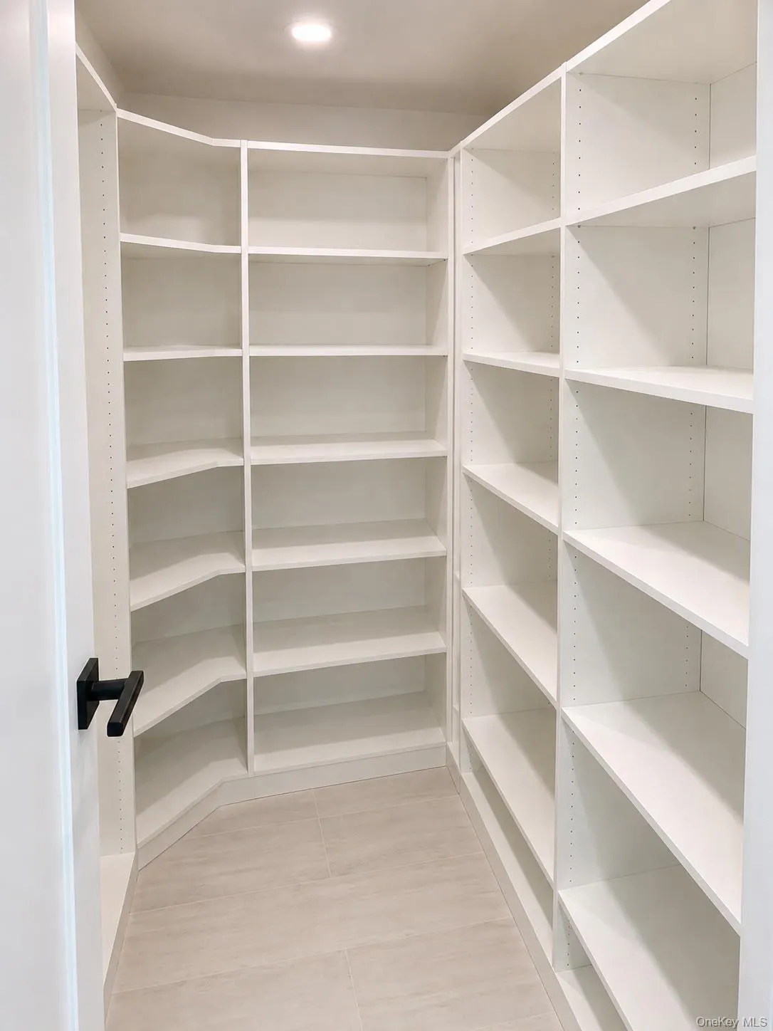 Walk-in pantry featuring extensive white built-in shelving, recessed ceiling lighting, and light-toned tile flooring Walk-in pantry featuring extensive white built-in shelving, recessed ceiling lighting, and light-toned tile flooring