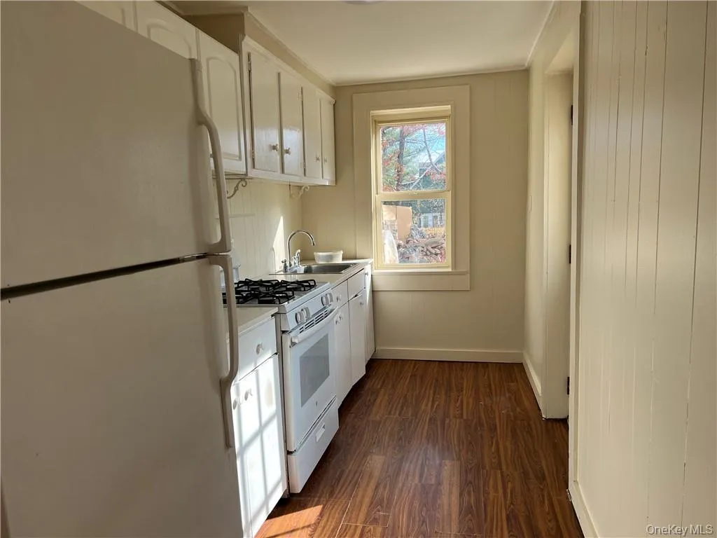 Kitchen with white cabinets, dark wood-type flooring, sink, and white appliances Kitchen with white cabinets, dark wood-type flooring, sink, and white appliances