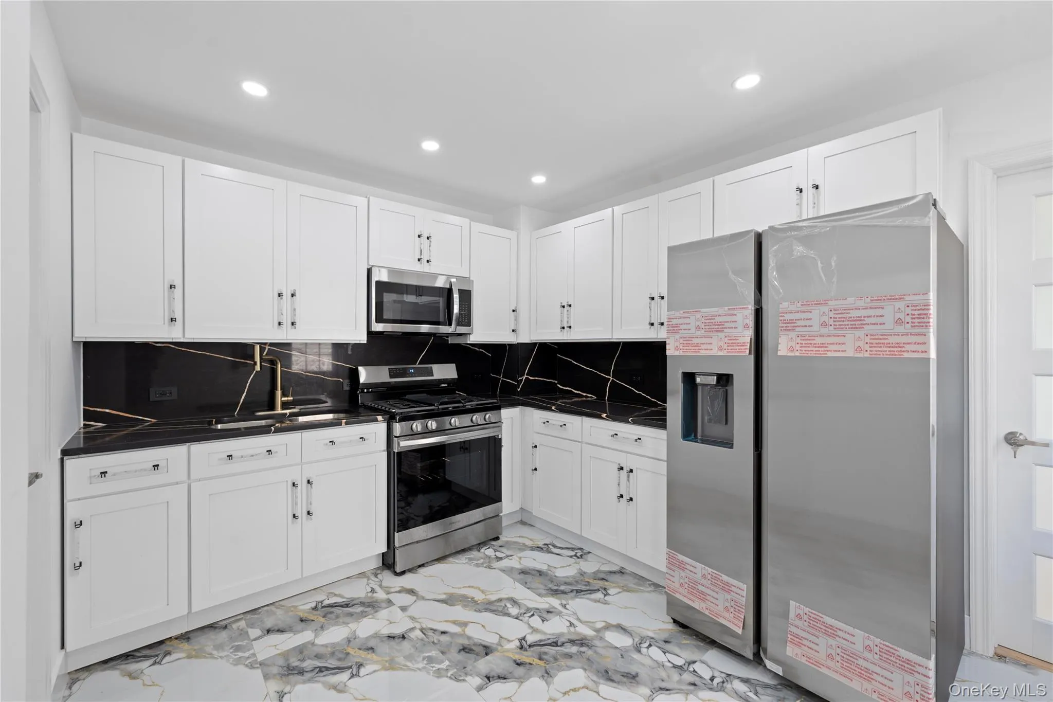 White cabinetry, black countertops with white veining, stainless steel appliances, and recessed lighting White cabinetry, black countertops with white veining, stainless steel appliances, and recessed lighting