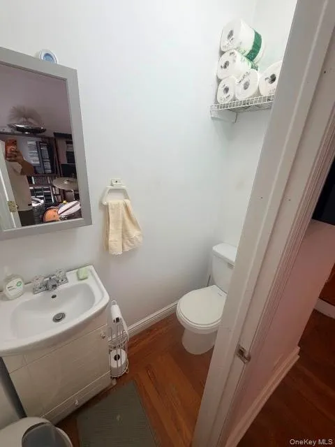 White single vanity with a rectangular sink, wall-mounted mirror, white commode, and wood-finish flooring White single vanity with a rectangular sink, wall-mounted mirror, white commode, and wood-finish flooring