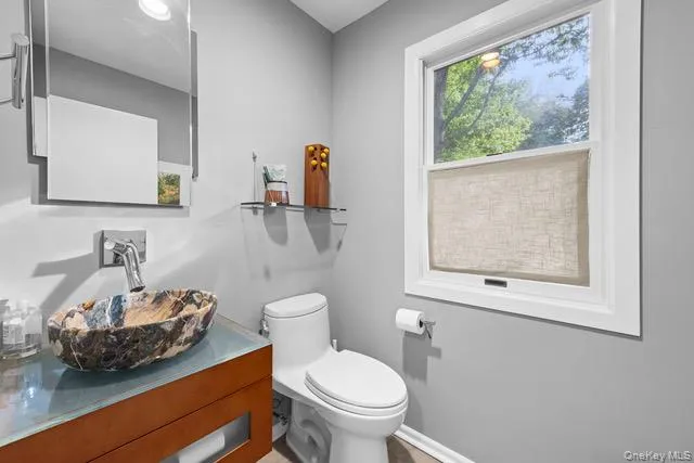 Vessel sink with a unique stone basin, wall-mounted faucet, wood-finish vanity, and a large window Vessel sink with a unique stone basin, wall-mounted faucet, wood-finish vanity, and a large window