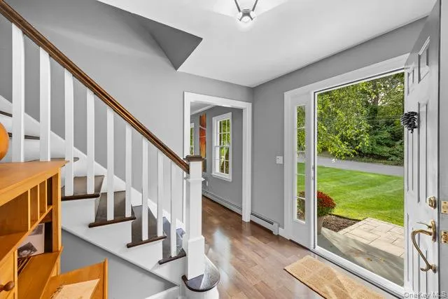 Wood-finish flooring, staircase with white risers and wood treads, white banister with wood handrail, paneled door with glass insert, and a stone paver entryway Wood-finish flooring, staircase with white risers and wood treads, white banister with wood handrail, paneled door with glass insert, and a stone paver entryway