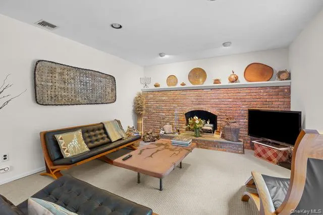 Brick-faced fireplace with an arched opening, recessed lighting, and light-colored carpeting Brick-faced fireplace with an arched opening, recessed lighting, and light-colored carpeting
