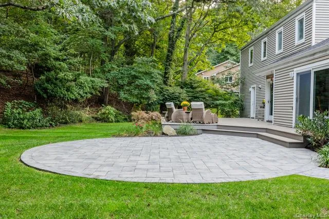 Expansive lawn with a circular paver patio, composite deck, and mature landscaping Expansive lawn with a circular paver patio, composite deck, and mature landscaping