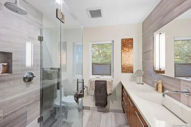 Full bathroom featuring a glass-enclosed shower with a rain showerhead, a built-in shower niche, a wood-finish vanity with an integrated rectangular sink, and a large wall-mounted mirror Full bathroom featuring a glass-enclosed shower with a rain showerhead, a built-in shower niche, a wood-finish vanity with an integrated rectangular sink, and a large wall-mounted mirror