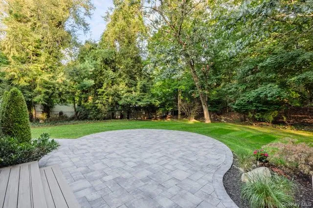 Expansive backyard featuring a curved paver patio, lush green lawn, and mature trees Expansive backyard featuring a curved paver patio, lush green lawn, and mature trees