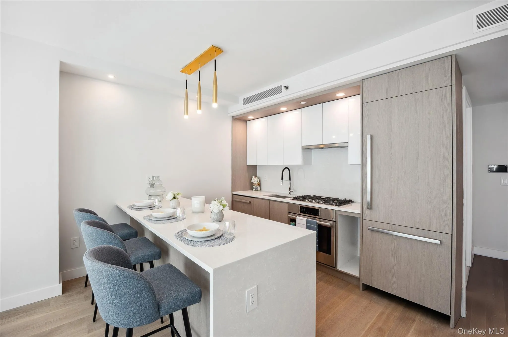 Kitchen featuring appliances with stainless steel finishes, a kitchen bar, modern cabinets, light wood-type flooring, and light countertops Kitchen featuring appliances with stainless steel finishes, a kitchen bar, modern cabinets, light wood-type flooring, and light countertops