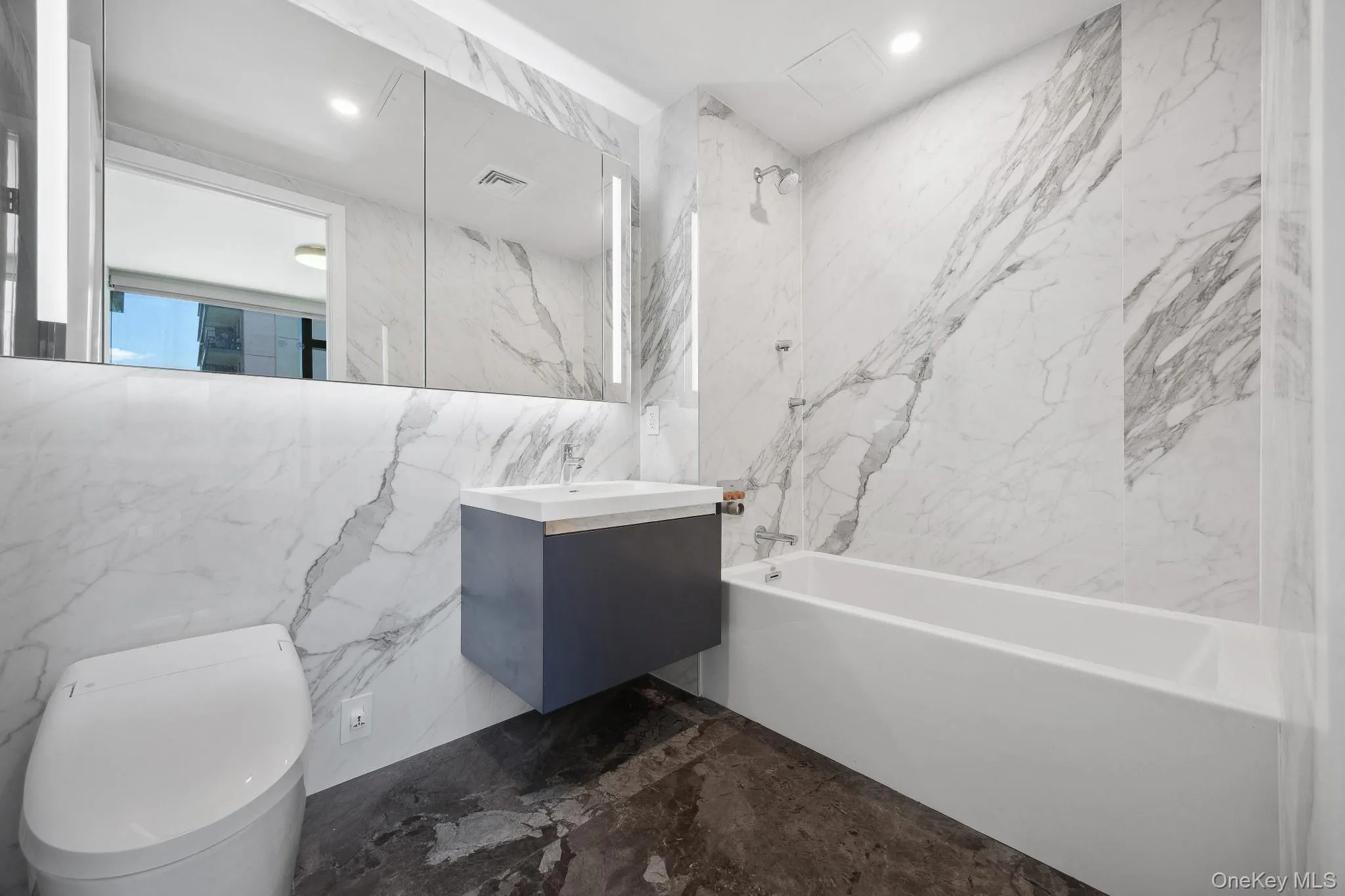 Full bathroom featuring shower / bath combination, marble tiled flooring, vanity, toilet, and tile walls Full bathroom featuring shower / bath combination, marble tiled flooring, vanity, toilet, and tile walls