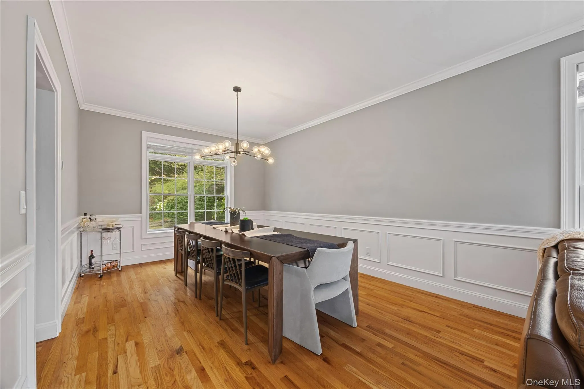 Dining space featuring crown molding, light wood-style floors, a chandelier, a wainscoted wall, and a decorative wall Dining space featuring crown molding, light wood-style floors, a chandelier, a wainscoted wall, and a decorative wall