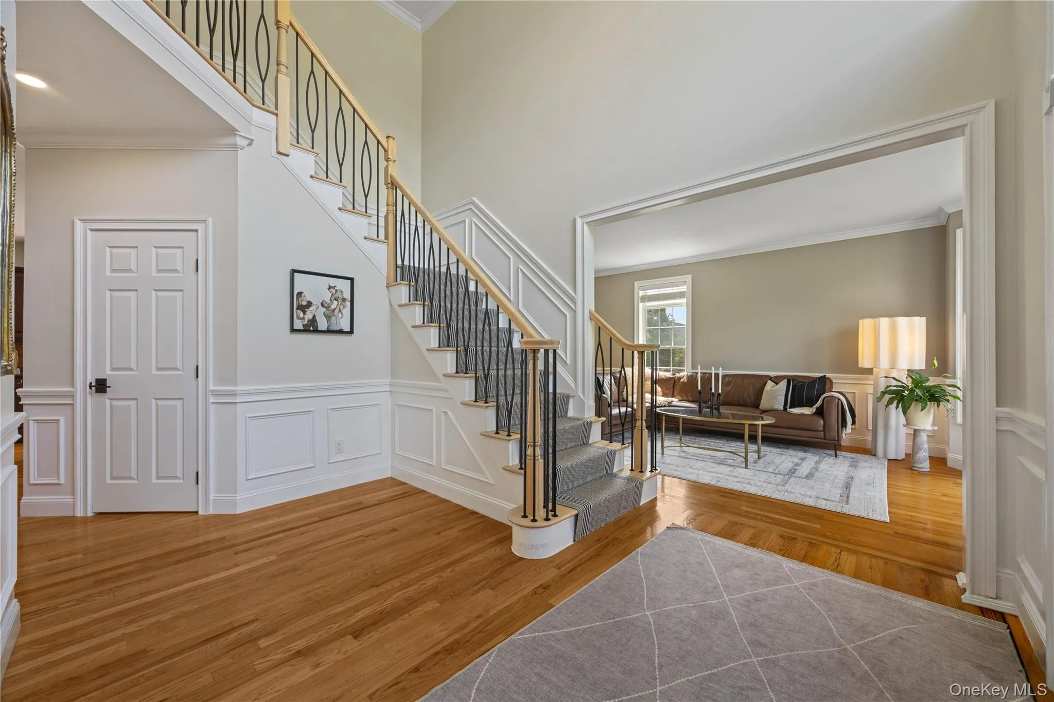 Foyer entrance with crown molding, light wood finished floors, wainscoting, a decorative wall, and stairs Foyer entrance with crown molding, light wood finished floors, wainscoting, a decorative wall, and stairs