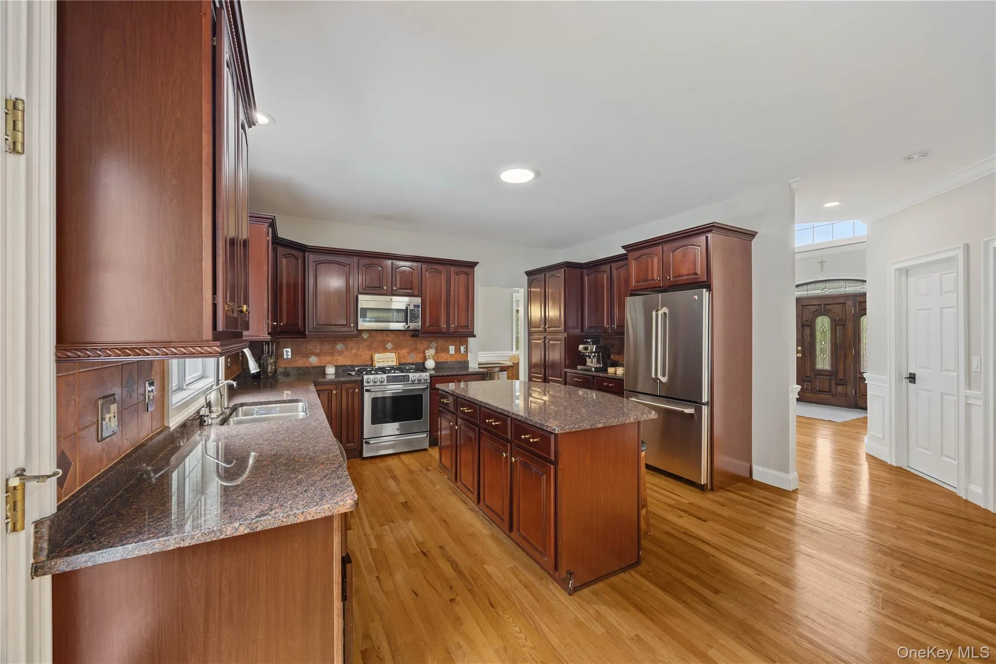 Kitchen with backsplash, a center island, stainless steel appliances, dark stone counters, and light wood-type flooring Kitchen with backsplash, a center island, stainless steel appliances, dark stone counters, and light wood-type flooring