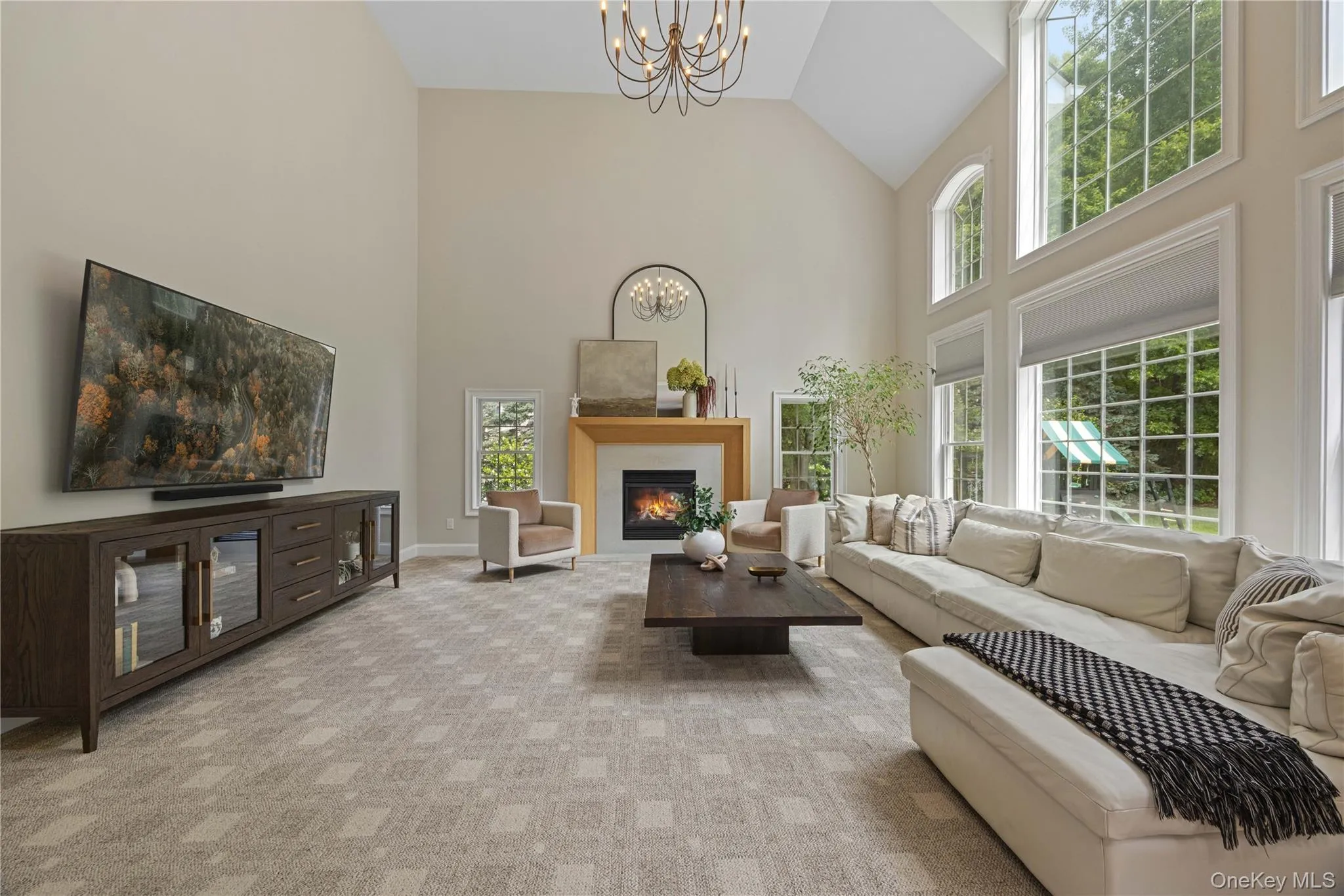 Living area with a chandelier, light colored carpet, a glass covered fireplace, and high vaulted ceiling Living area with a chandelier, light colored carpet, a glass covered fireplace, and high vaulted ceiling