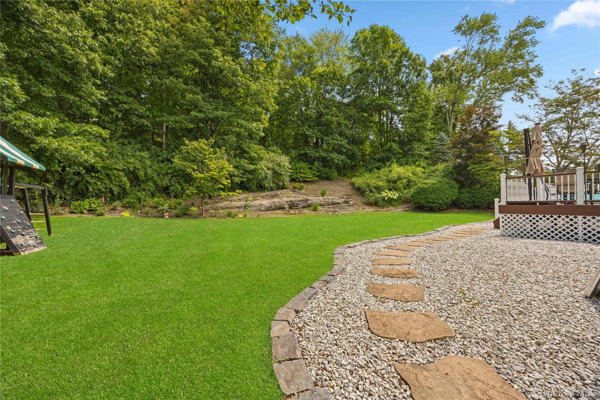 View of grassy yard featuring a wooden deck and view of wooded area View of grassy yard featuring a wooden deck and view of wooded area