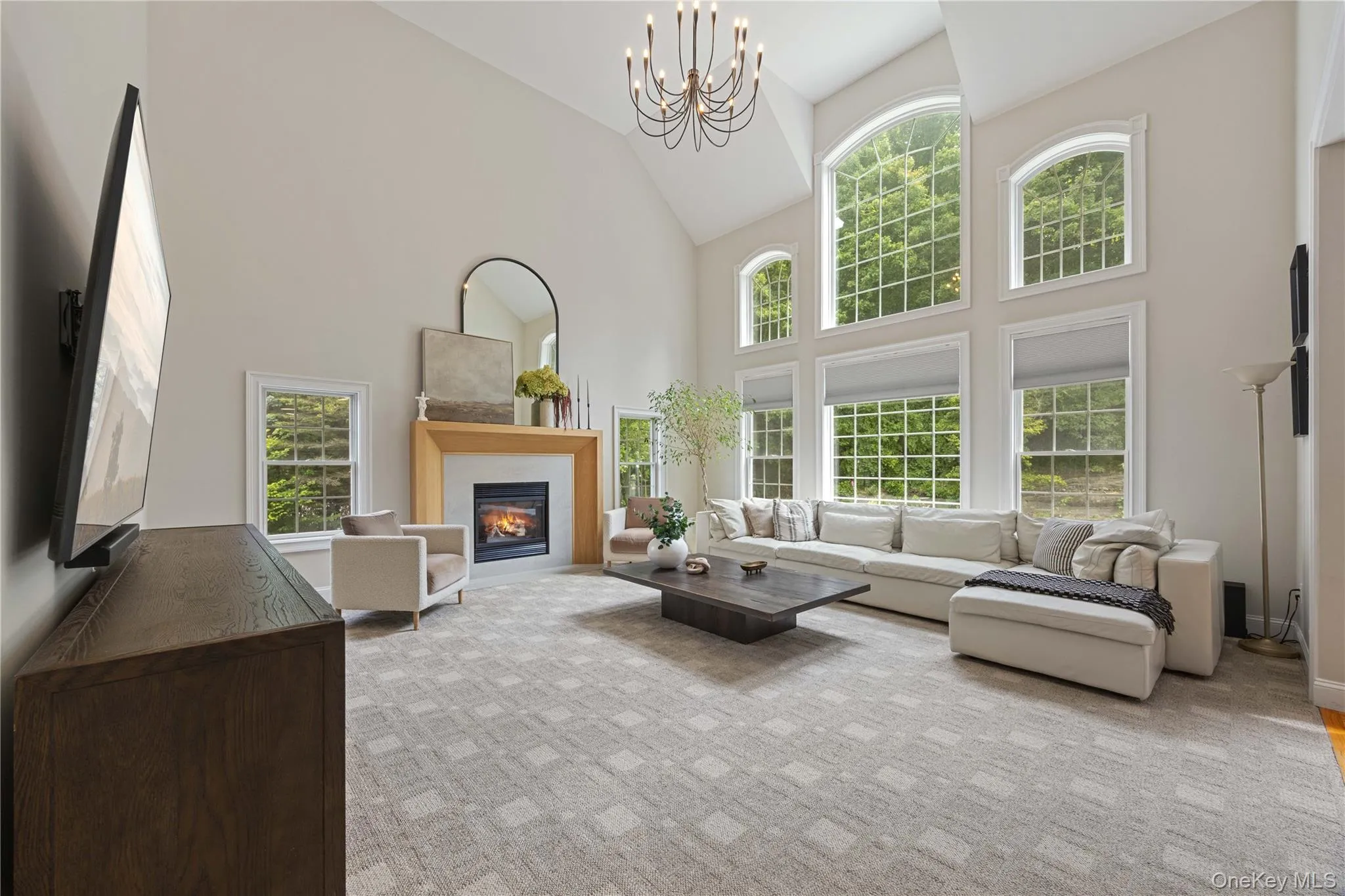 Living area with a glass covered fireplace, high vaulted ceiling, a chandelier, and light colored carpet Living area with a glass covered fireplace, high vaulted ceiling, a chandelier, and light colored carpet