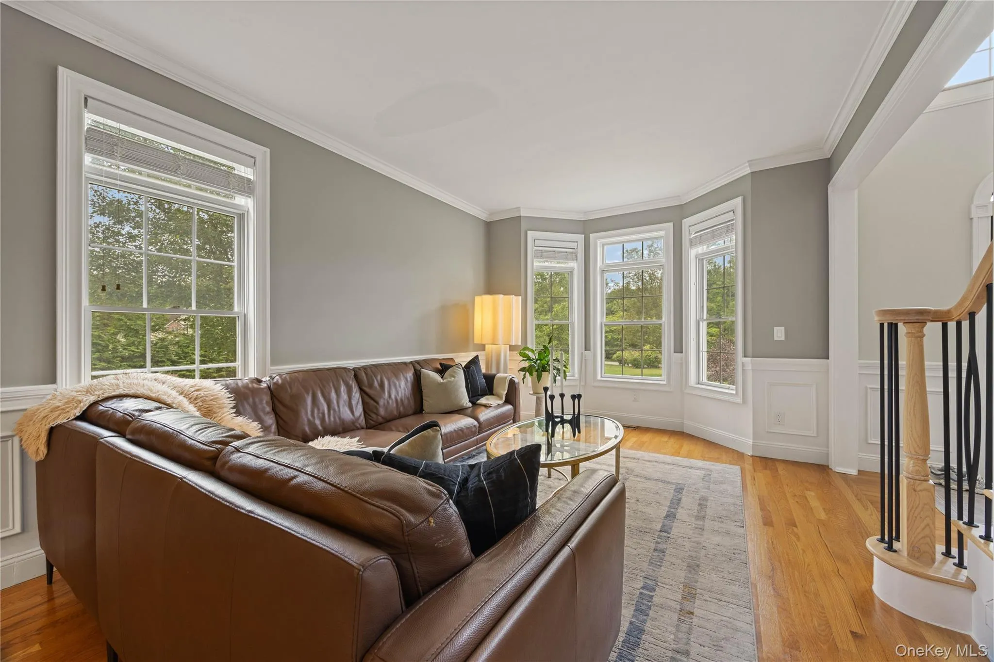 Living room featuring ornamental molding, stairway, light wood-type flooring, wainscoting, and a decorative wall Living room featuring ornamental molding, stairway, light wood-type flooring, wainscoting, and a decorative wall