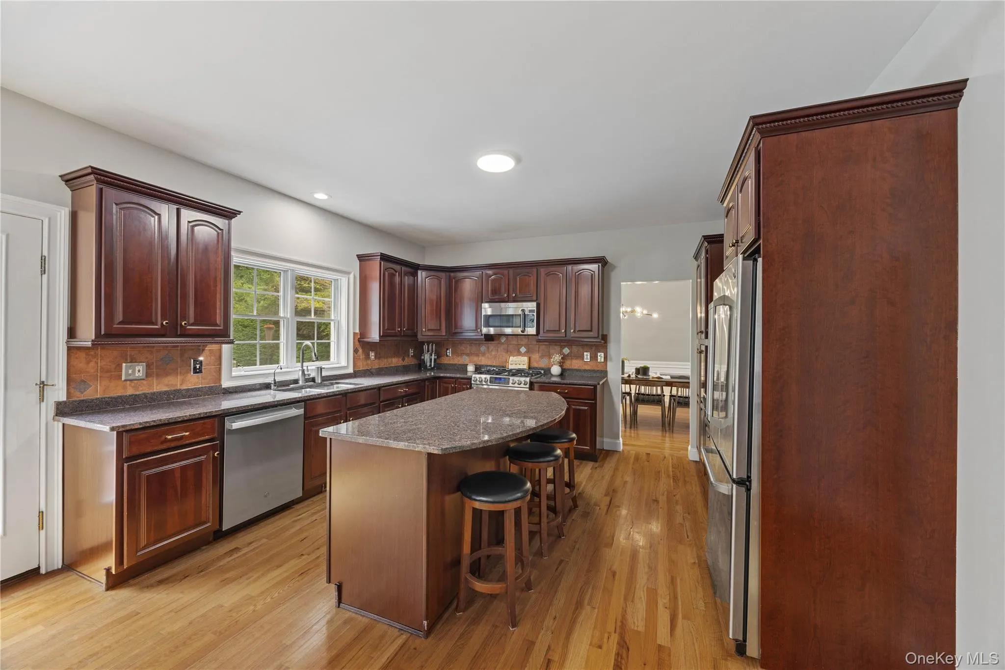 Kitchen featuring decorative backsplash, a kitchen bar, light wood finished floors, stainless steel appliances, and dark brown cabinets Kitchen featuring decorative backsplash, a kitchen bar, light wood finished floors, stainless steel appliances, and dark brown cabinets