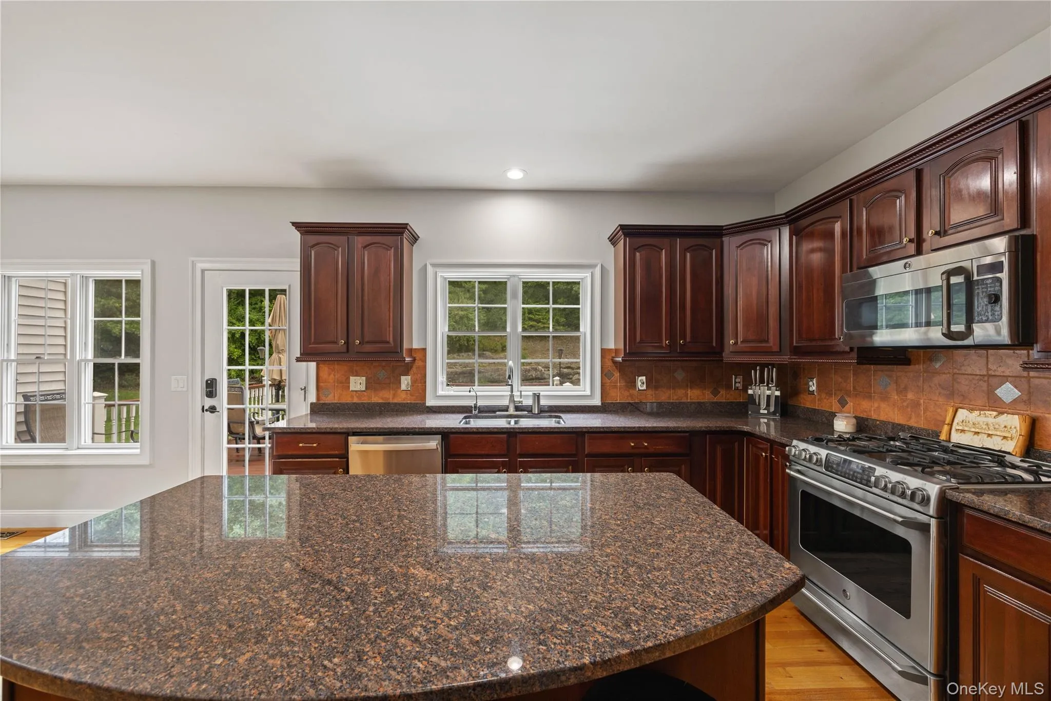 Kitchen with tasteful backsplash, appliances with stainless steel finishes, dark brown cabinetry, dark stone counters, and recessed lighting Kitchen with tasteful backsplash, appliances with stainless steel finishes, dark brown cabinetry, dark stone counters, and recessed lighting
