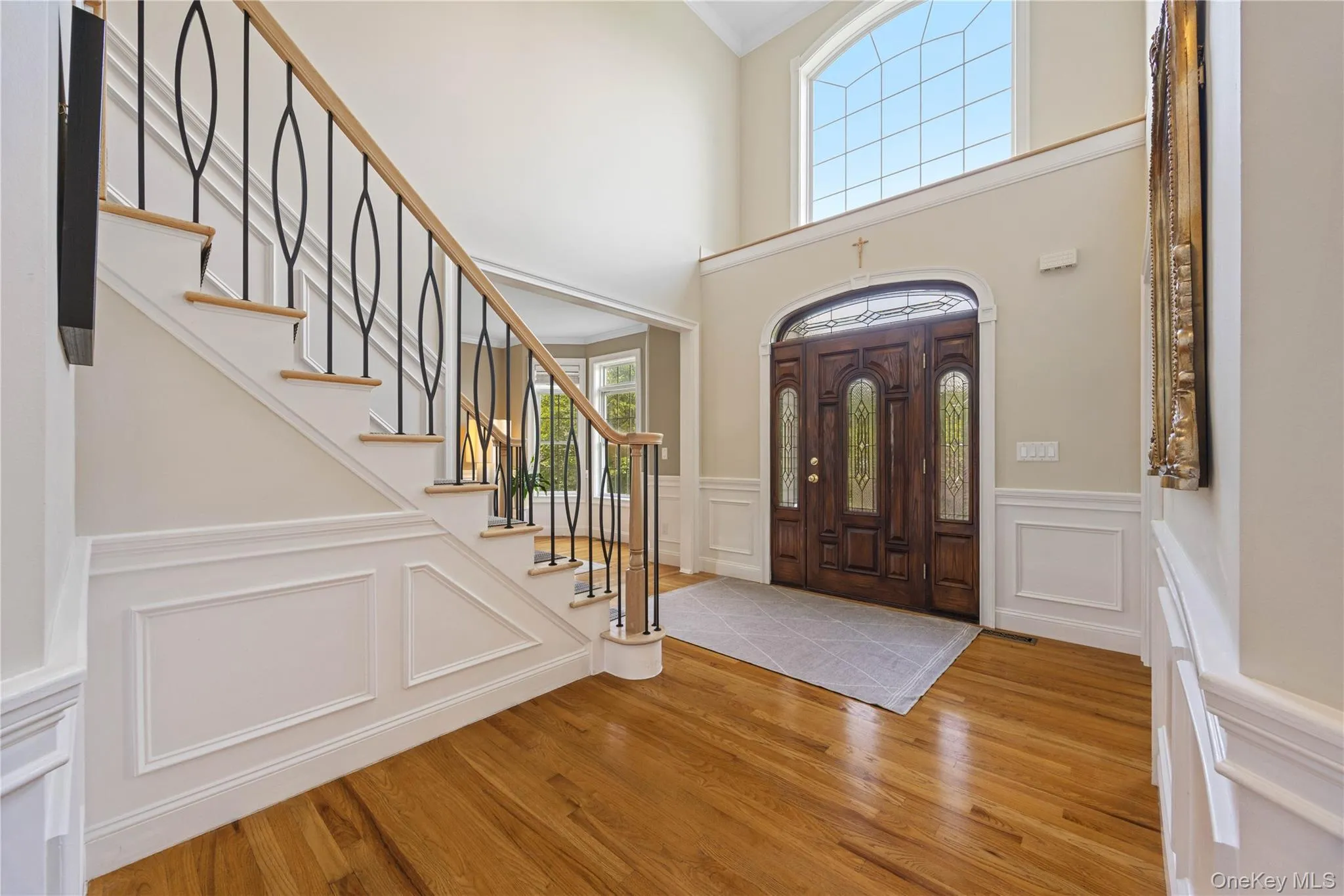 Entrance foyer with light wood-style flooring, a decorative wall, stairs, ornamental molding, and wainscoting Entrance foyer with light wood-style flooring, a decorative wall, stairs, ornamental molding, and wainscoting