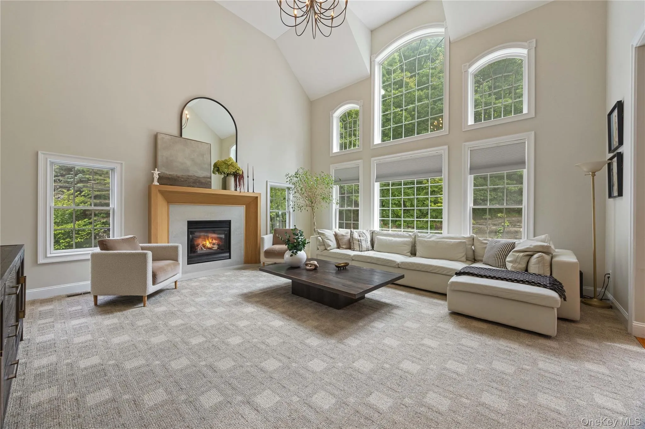 Living area with high vaulted ceiling, a glass covered fireplace, light colored carpet, and a chandelier Living area with high vaulted ceiling, a glass covered fireplace, light colored carpet, and a chandelier