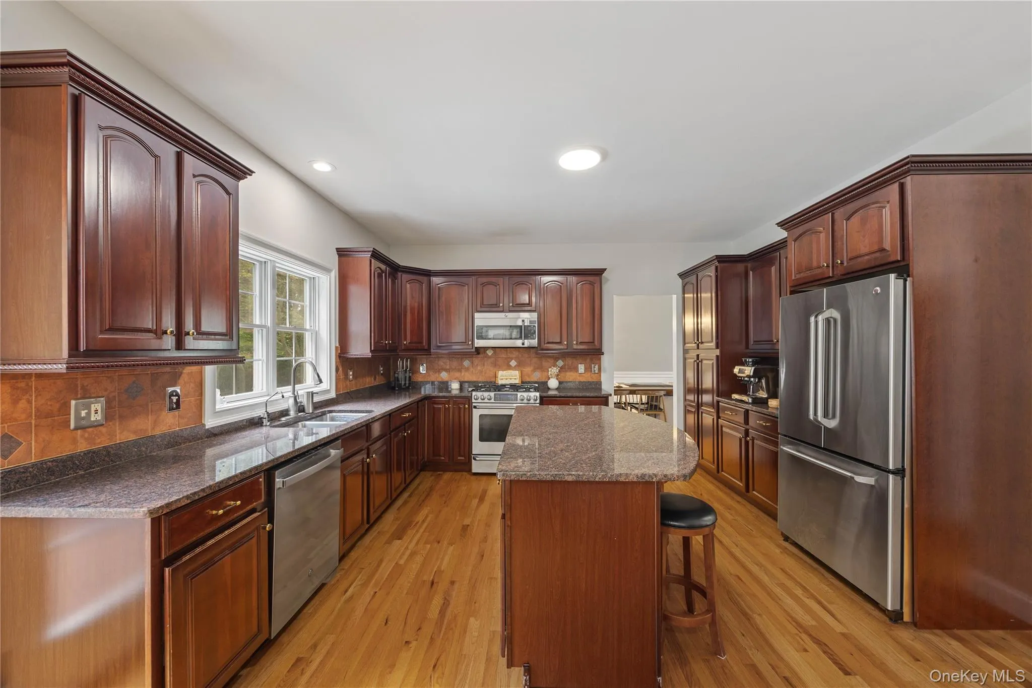 Kitchen with stainless steel appliances, a breakfast bar, light wood-style floors, backsplash, and a kitchen island Kitchen with stainless steel appliances, a breakfast bar, light wood-style floors, backsplash, and a kitchen island