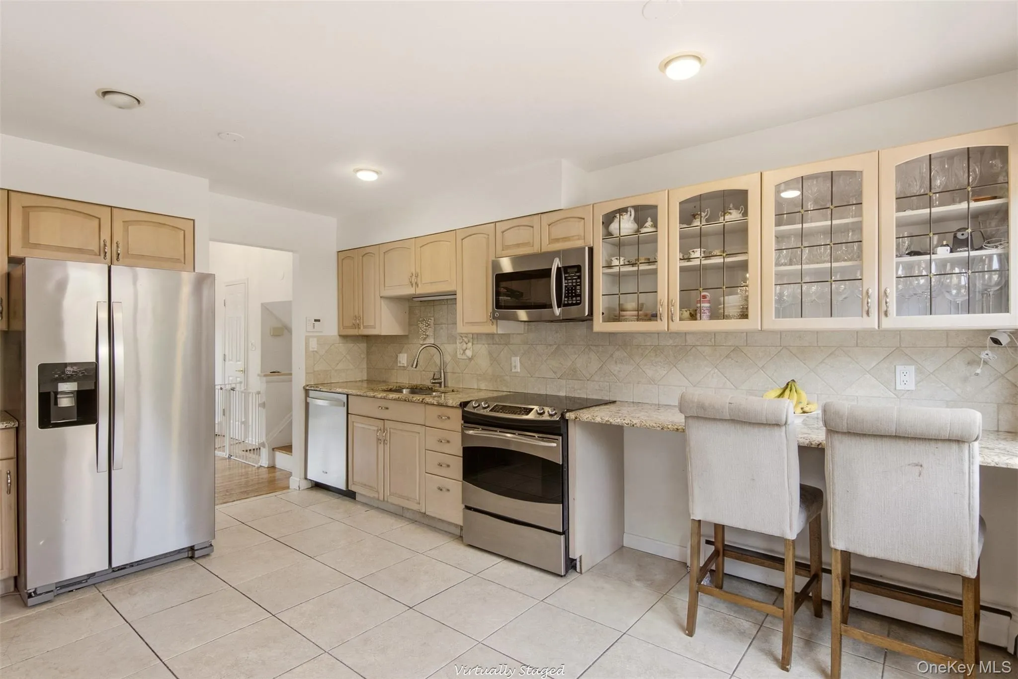 Kitchen featuring stainless steel appliances, light-toned cabinetry, a built-in breakfast bar, granite countertops, and tiled flooring Kitchen featuring stainless steel appliances, light-toned cabinetry, a built-in breakfast bar, granite countertops, and tiled flooring