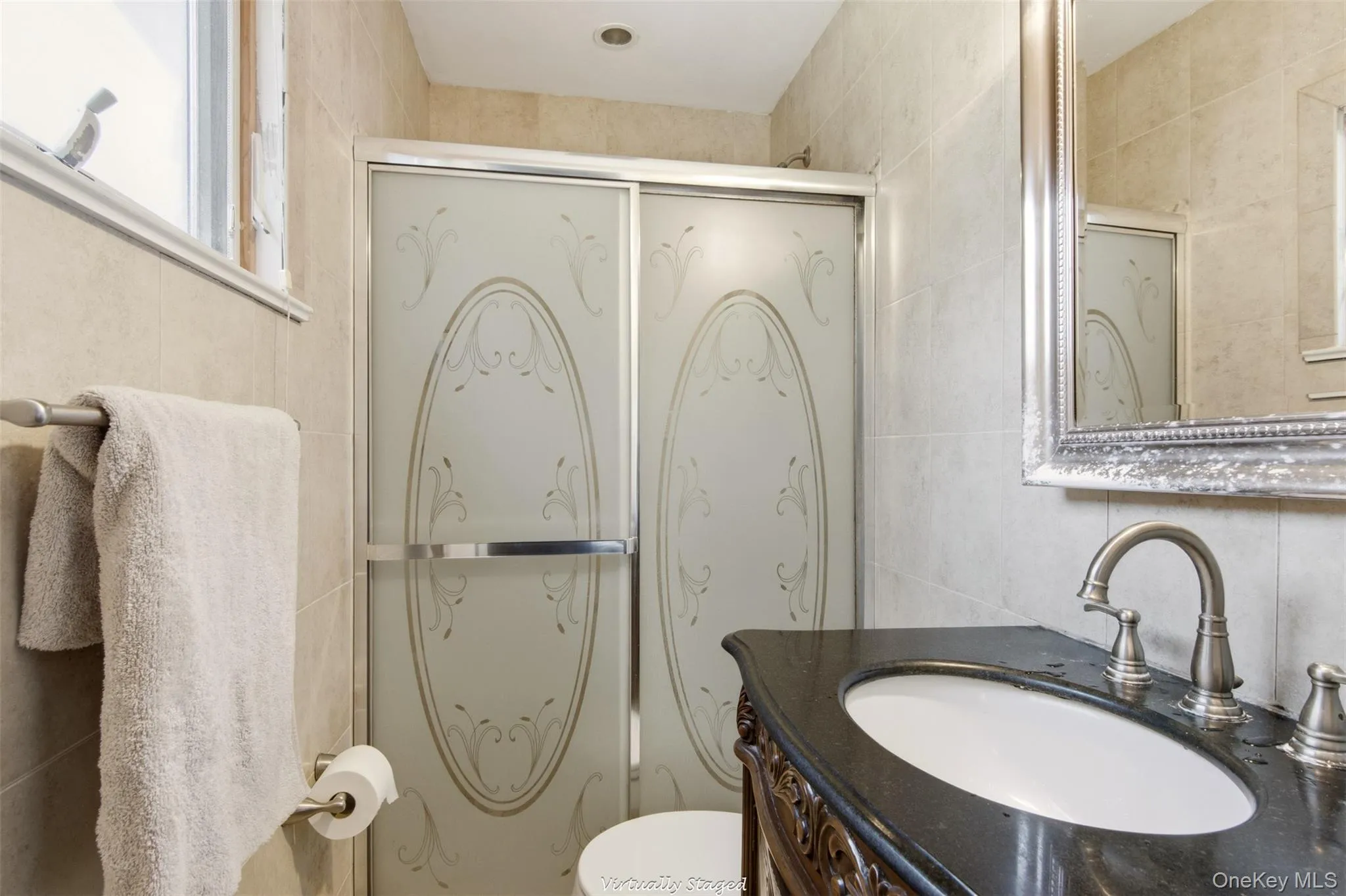 Shower with decorative frosted glass doors, dark countertop vanity with an oval sink, brushed nickel faucet, and a wall-mounted mirror with an ornate frame Shower with decorative frosted glass doors, dark countertop vanity with an oval sink, brushed nickel faucet, and a wall-mounted mirror with an ornate frame