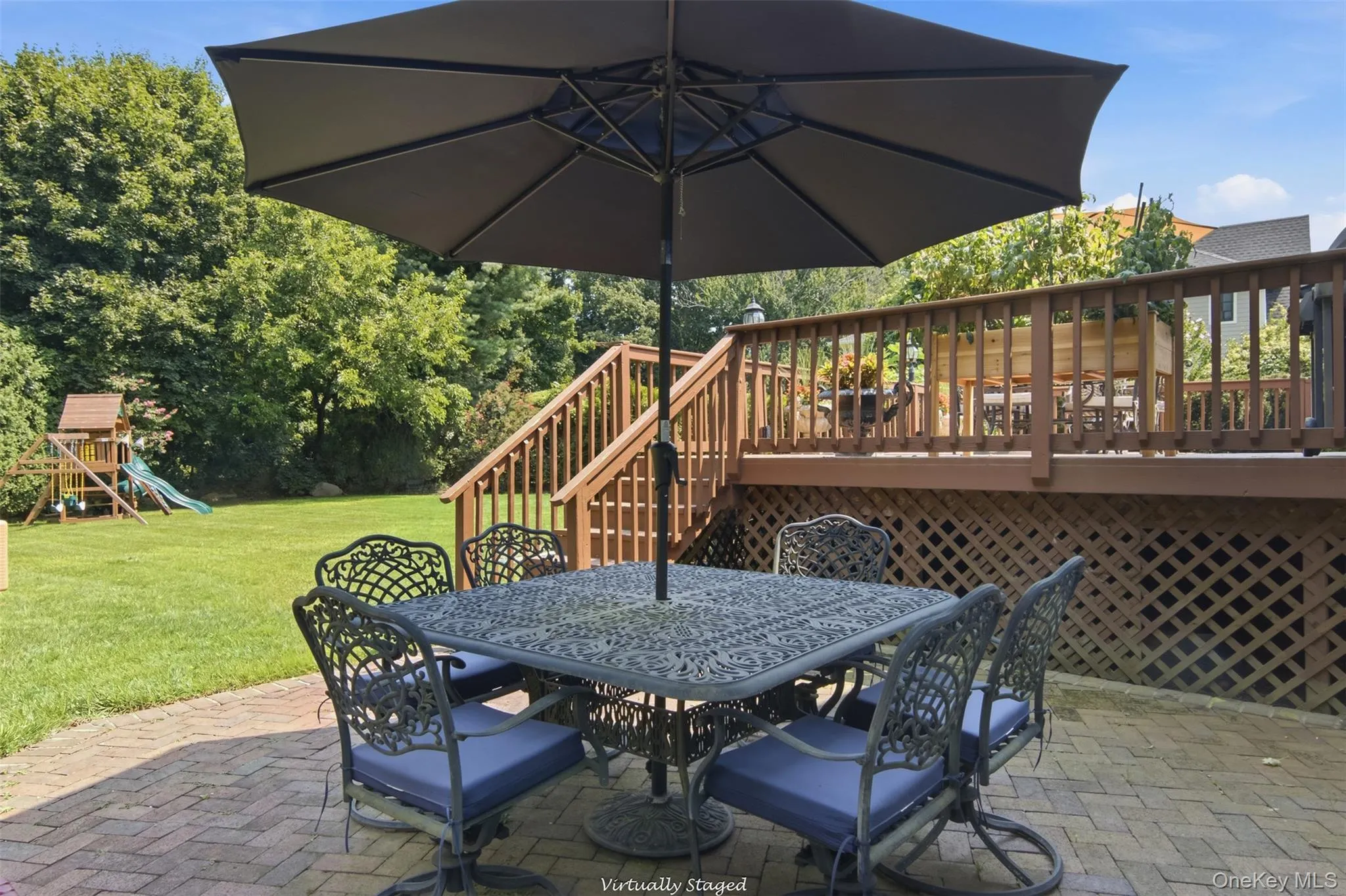 Brick paver patio with a wood deck, wood railings, and lattice skirting, featuring a spacious grass yard Brick paver patio with a wood deck, wood railings, and lattice skirting, featuring a spacious grass yard