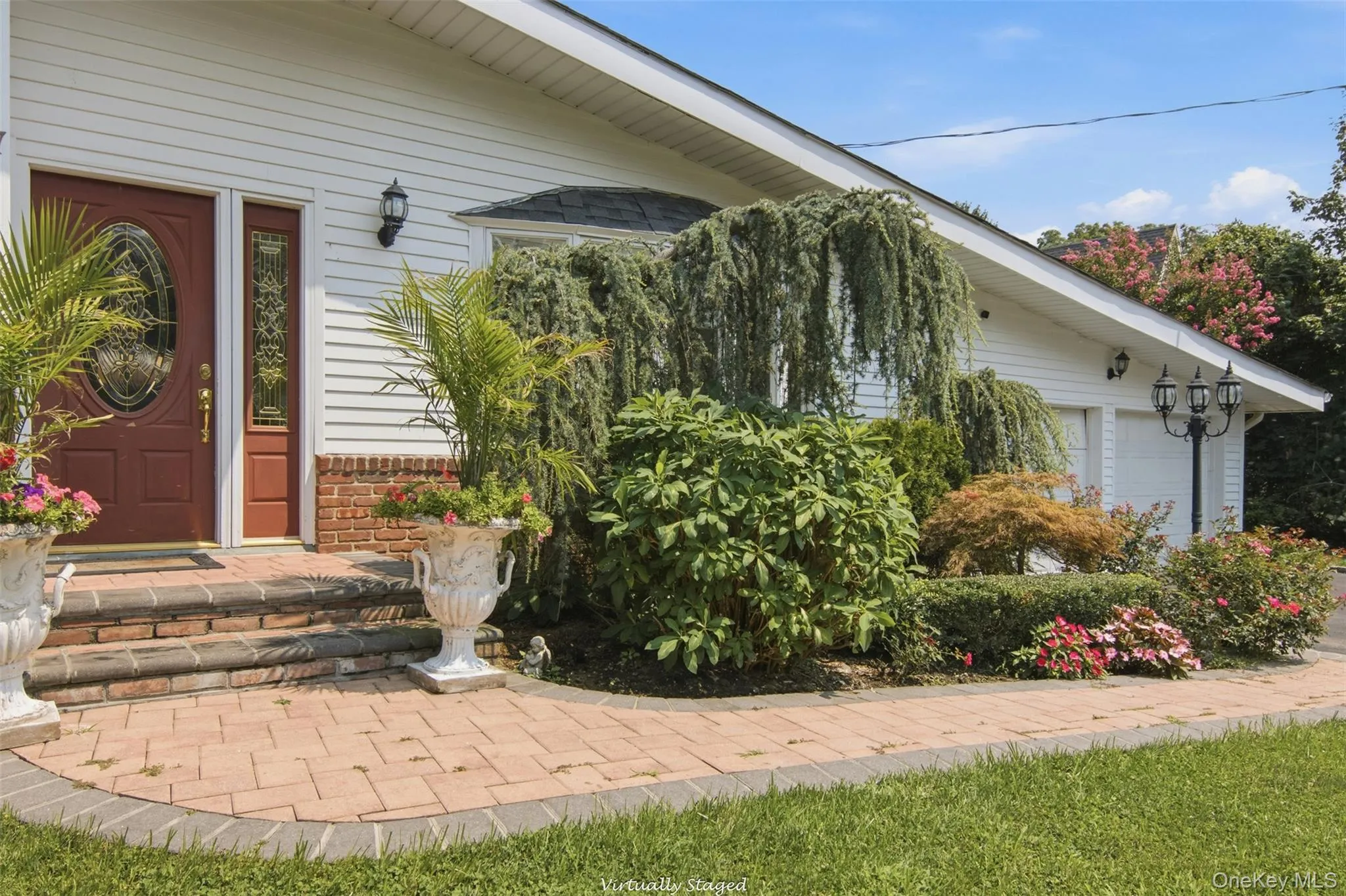 Brick paver walkway with a brick step entry, white siding exterior, and an attached two-car garage Brick paver walkway with a brick step entry, white siding exterior, and an attached two-car garage