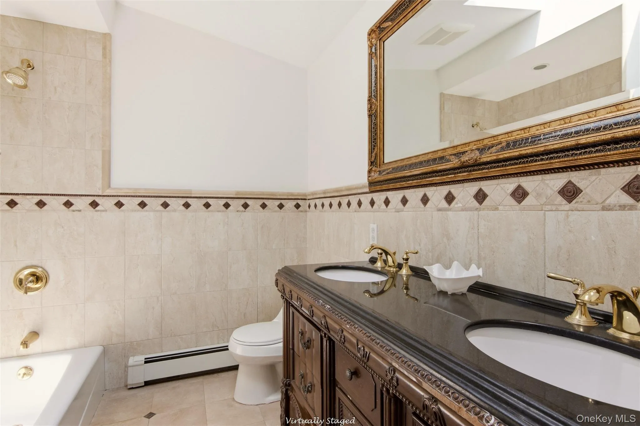 Dual vanity with dark countertop, ornate wood-finish cabinetry, and gold-tone fixtures Dual vanity with dark countertop, ornate wood-finish cabinetry, and gold-tone fixtures