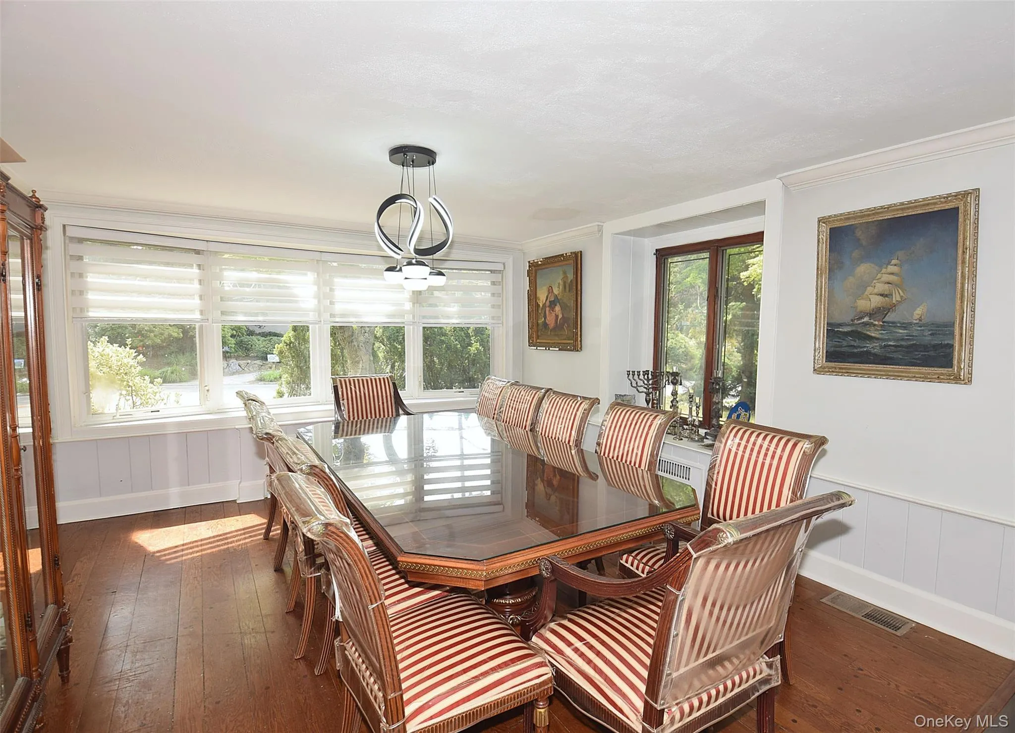 Wood-finish flooring, white paneled lower walls, multiple windows, and a modern chandelier Wood-finish flooring, white paneled lower walls, multiple windows, and a modern chandelier