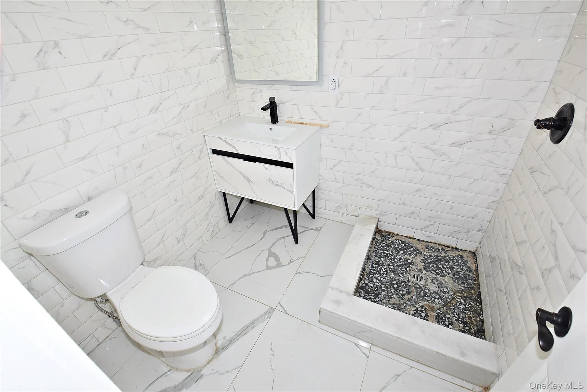 Modern bathroom featuring white tile walls, white tile flooring, a contemporary vanity with a wall-mounted faucet, and a shower area with pebble flooring Modern bathroom featuring white tile walls, white tile flooring, a contemporary vanity with a wall-mounted faucet, and a shower area with pebble flooring