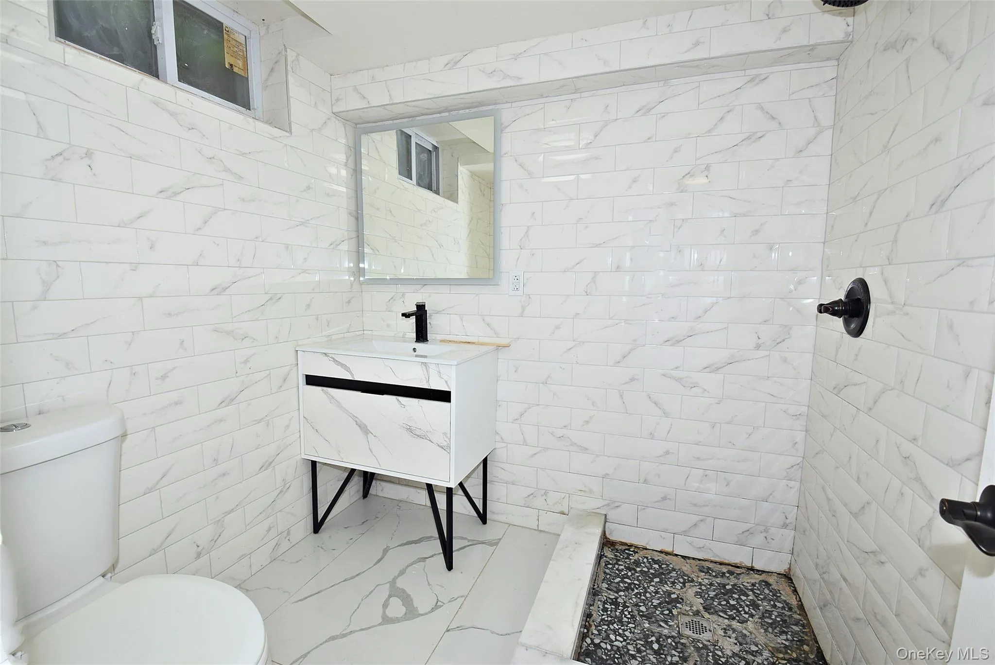 Tile flooring complements full-height tile walls, a modern vanity with integrated sink, and a black-finish faucet Tile flooring complements full-height tile walls, a modern vanity with integrated sink, and a black-finish faucet