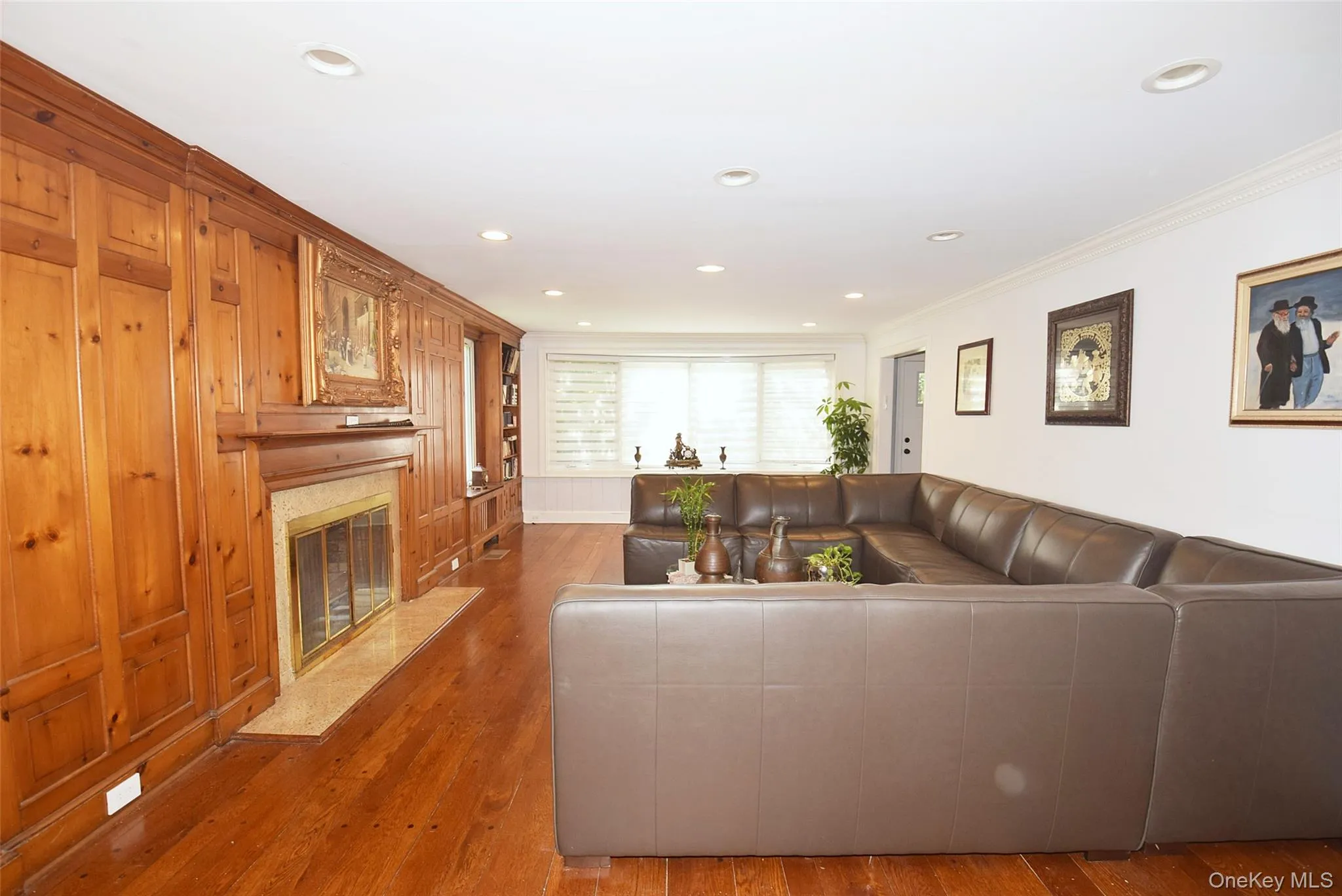Wood-paneled wall with integrated fireplace, rich wood-finish flooring, recessed lighting, and built-in shelving Wood-paneled wall with integrated fireplace, rich wood-finish flooring, recessed lighting, and built-in shelving