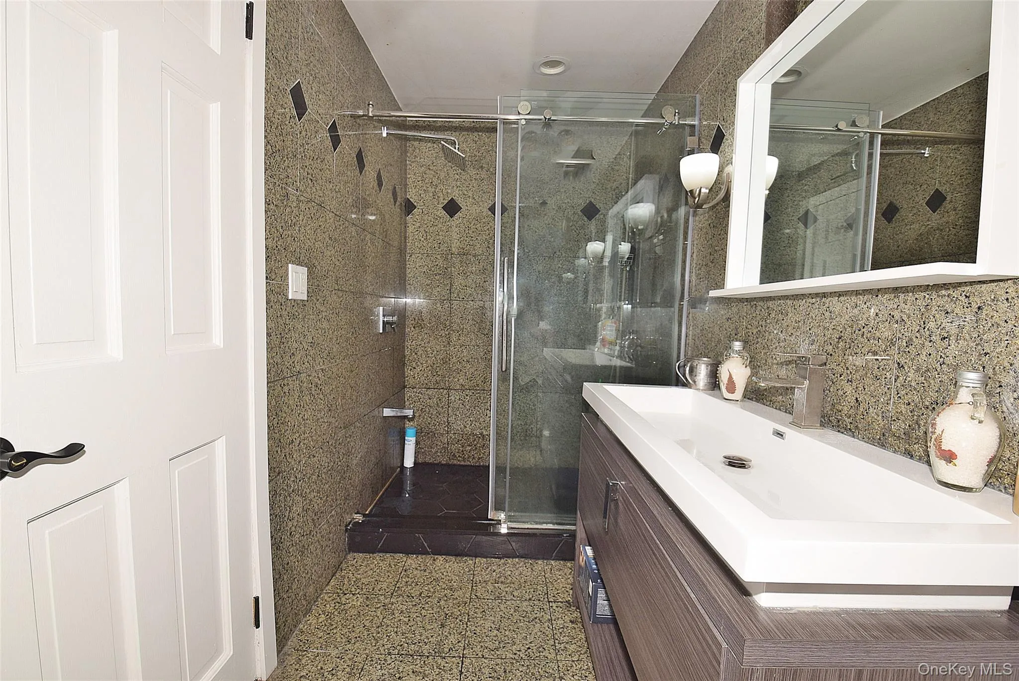 Floating vanity with integrated basin, brushed nickel faucet, mirrored medicine cabinet, and glass-enclosed shower with tile surround Floating vanity with integrated basin, brushed nickel faucet, mirrored medicine cabinet, and glass-enclosed shower with tile surround