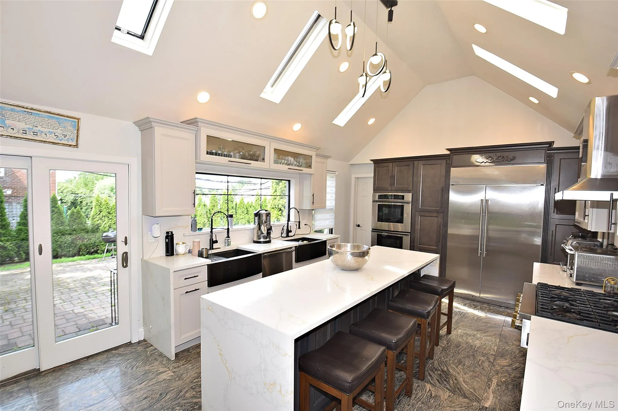 Vaulted ceiling with multiple skylights, extensive recessed lighting, stainless steel double-door refrigerator, integrated double wall oven, and a kitchen island with seating Vaulted ceiling with multiple skylights, extensive recessed lighting, stainless steel double-door refrigerator, integrated double wall oven, and a kitchen island with seating