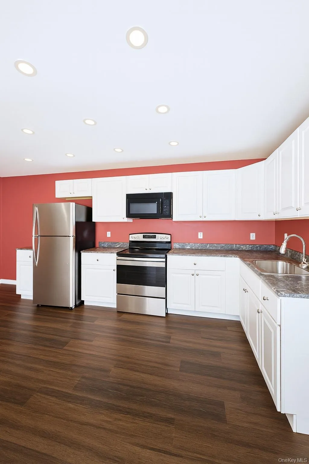 Kitchen featuring stainless steel appliances, white cabinets, recessed lighting, and dark wood-style floors Kitchen featuring stainless steel appliances, white cabinets, recessed lighting, and dark wood-style floors
