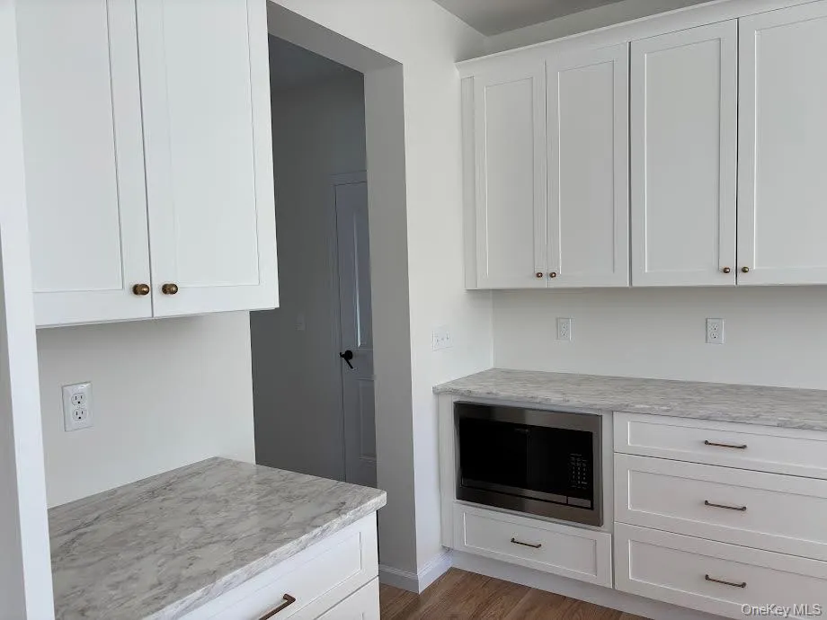 Kitchen with white cabinetry, built in microwave, light stone countertops, and wood-type flooring Kitchen with white cabinetry, built in microwave, light stone countertops, and wood-type flooring