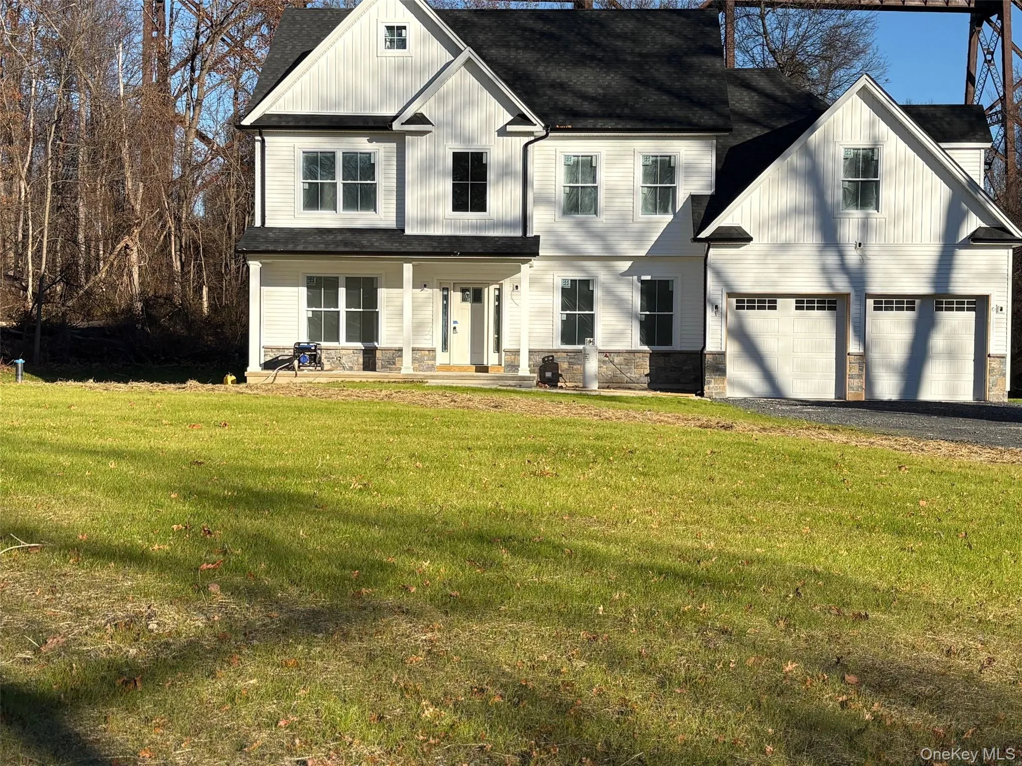 View of front facade featuring stone siding, a porch, a front yard, and a shingled roof View of front facade featuring stone siding, a porch, a front yard, and a shingled roof