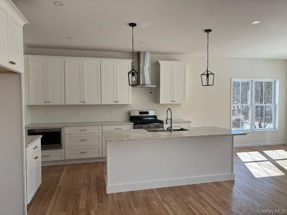 Kitchen with decorative light fixtures, wall chimney exhaust hood, and a kitchen island with sink Kitchen with decorative light fixtures, wall chimney exhaust hood, and a kitchen island with sink