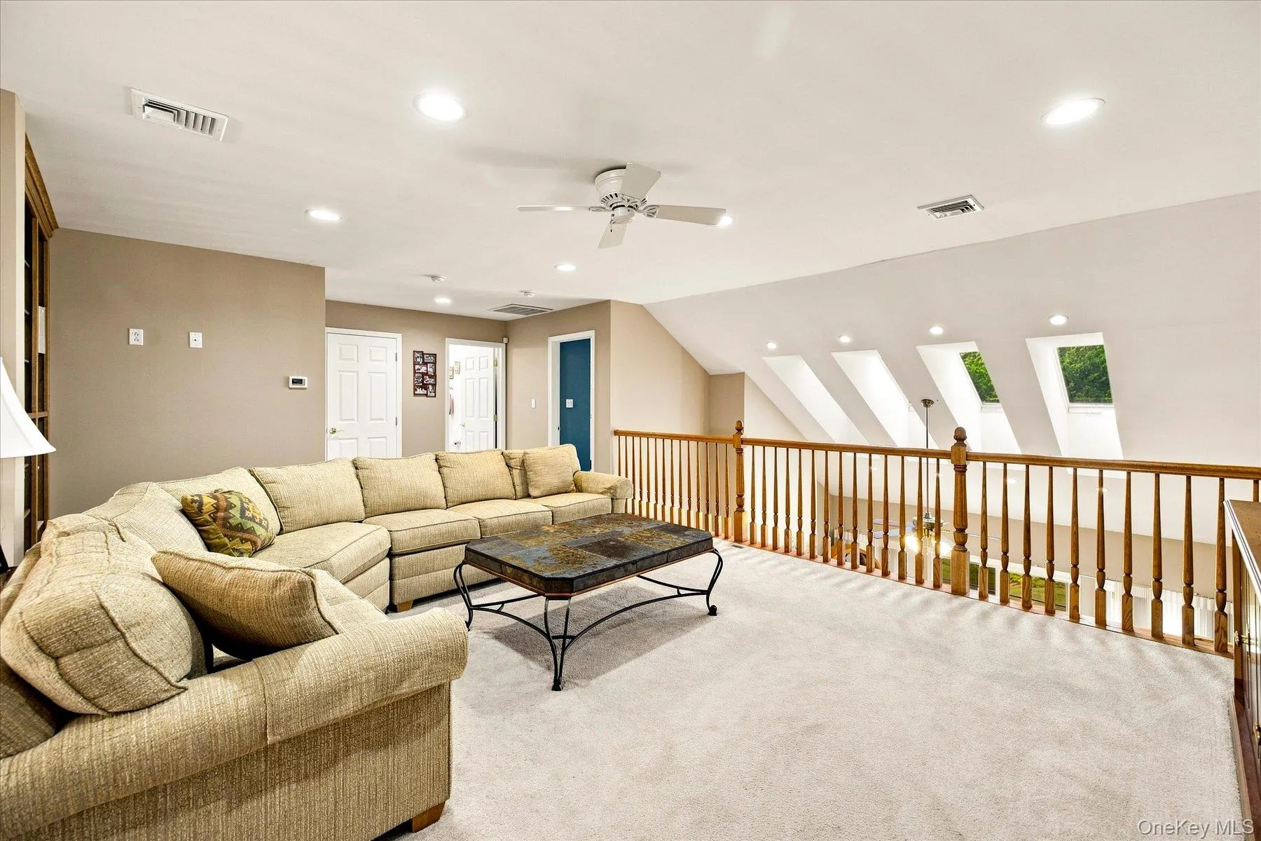 Spacious loft area featuring recessed lighting, a ceiling fan, a wood spindle railing, and multiple skylights Spacious loft area featuring recessed lighting, a ceiling fan, a wood spindle railing, and multiple skylights