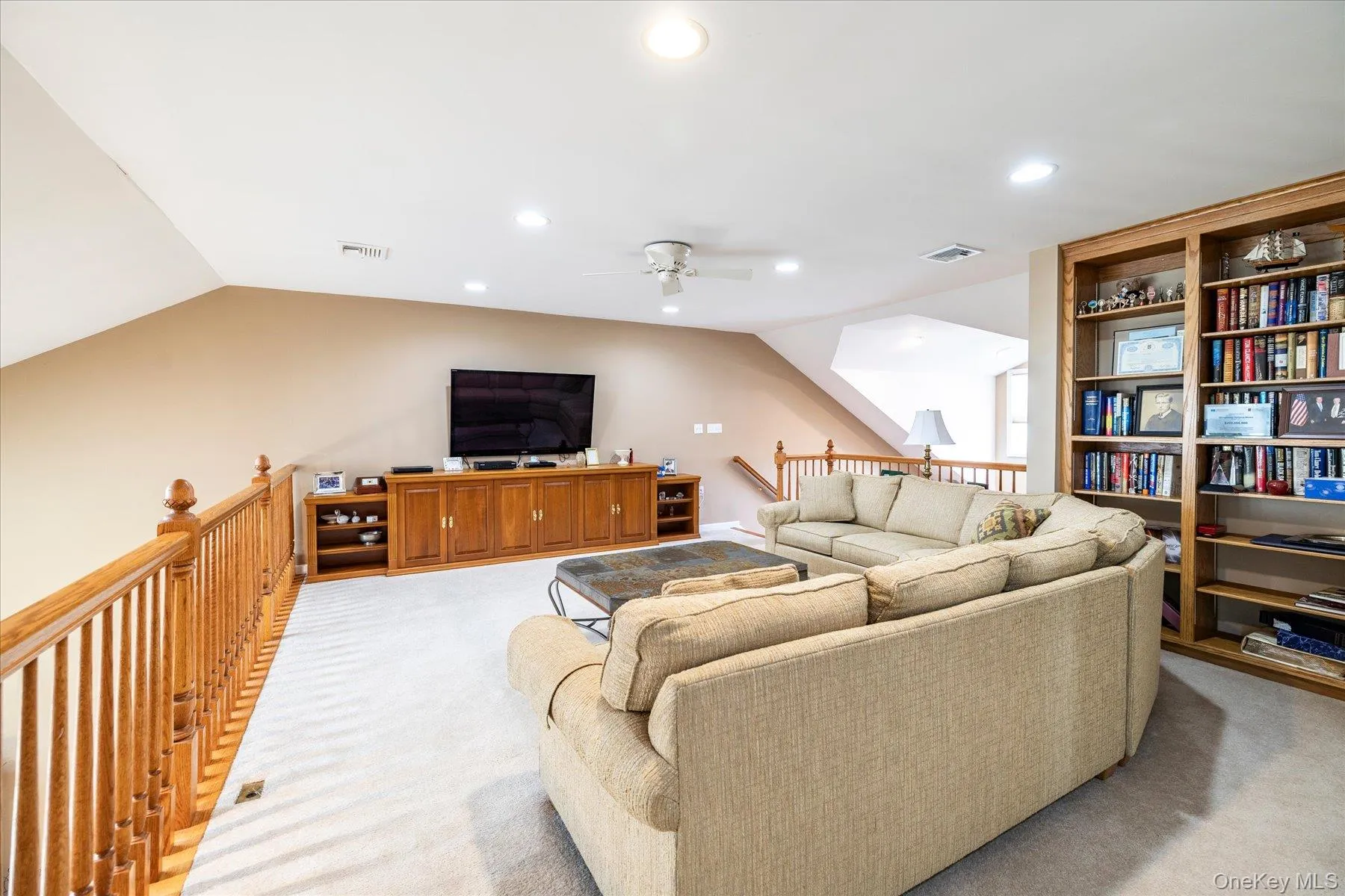 Vaulted ceiling with recessed lighting, integrated wood-finish entertainment center, built-in wood-finish shelving, and wood-finish railing Vaulted ceiling with recessed lighting, integrated wood-finish entertainment center, built-in wood-finish shelving, and wood-finish railing