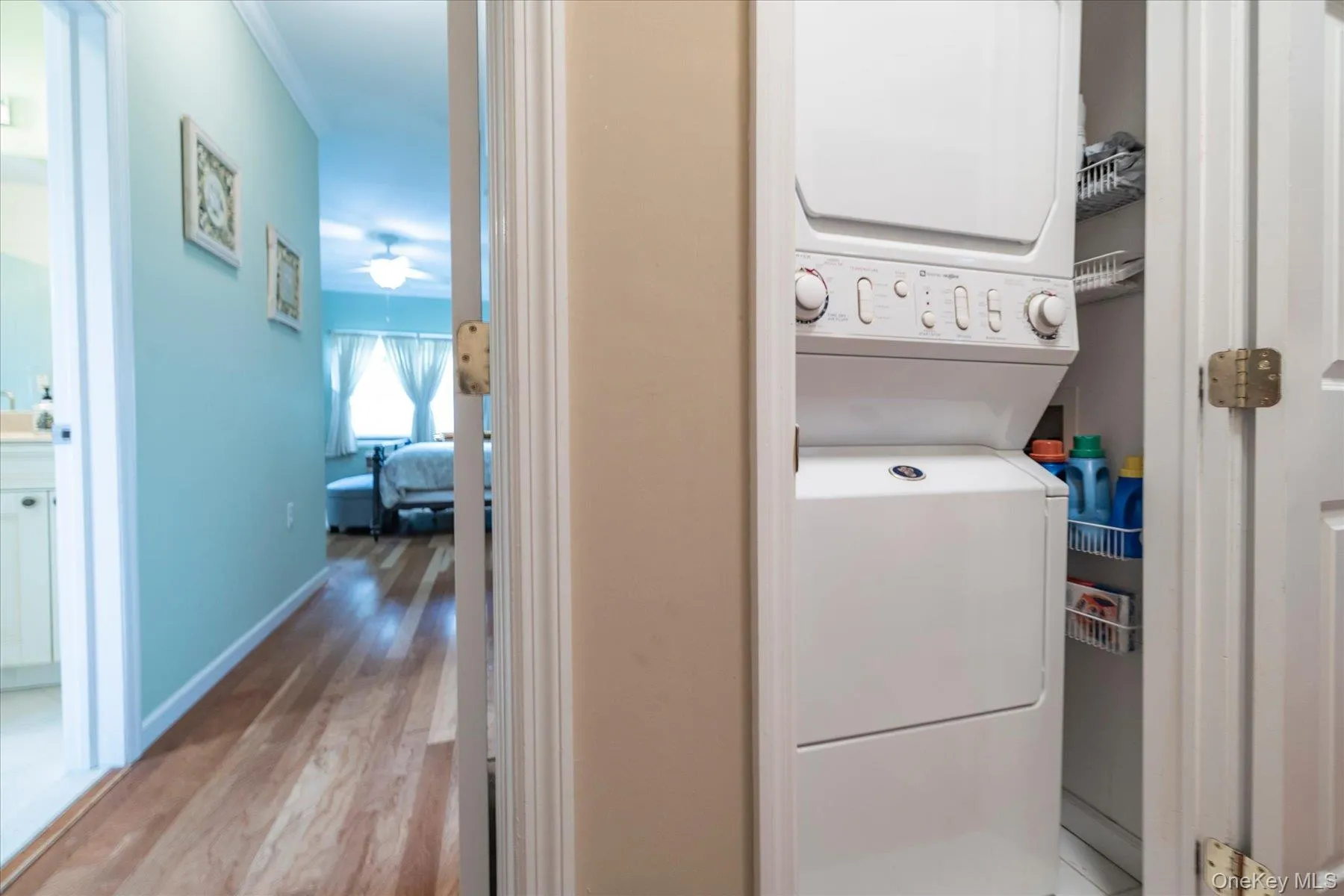 Built-in laundry closet with stacked washer and dryer unit, featuring wire shelving located in hallway off the primary suite Built-in laundry closet with stacked washer and dryer unit, featuring wire shelving located in hallway off the primary suite