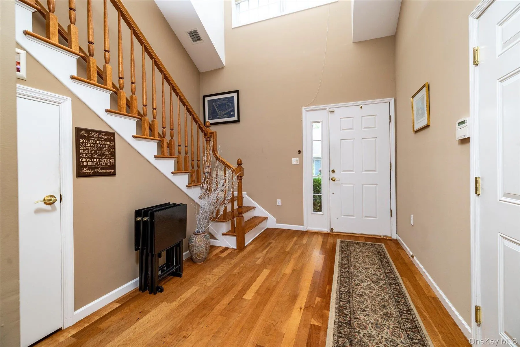 Wood-finish flooring, staircase with natural wood balusters, paneled entry door with sidelite, and an additional paneled door Wood-finish flooring, staircase with natural wood balusters, paneled entry door with sidelite, and an additional paneled door
