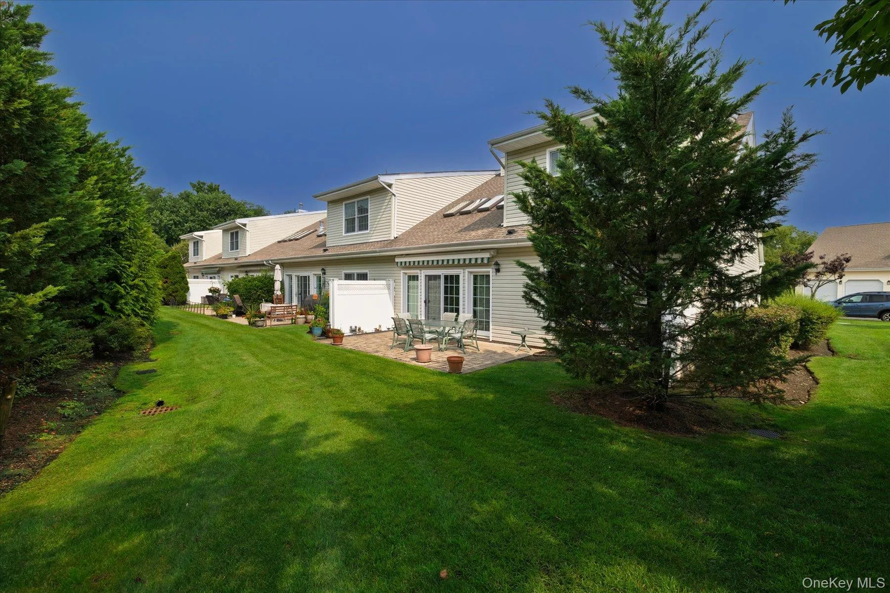 Expansive green lawn with mature landscaping, a paved patio, and a natural privacy fence Expansive green lawn with mature landscaping, a paved patio, and a natural privacy fence