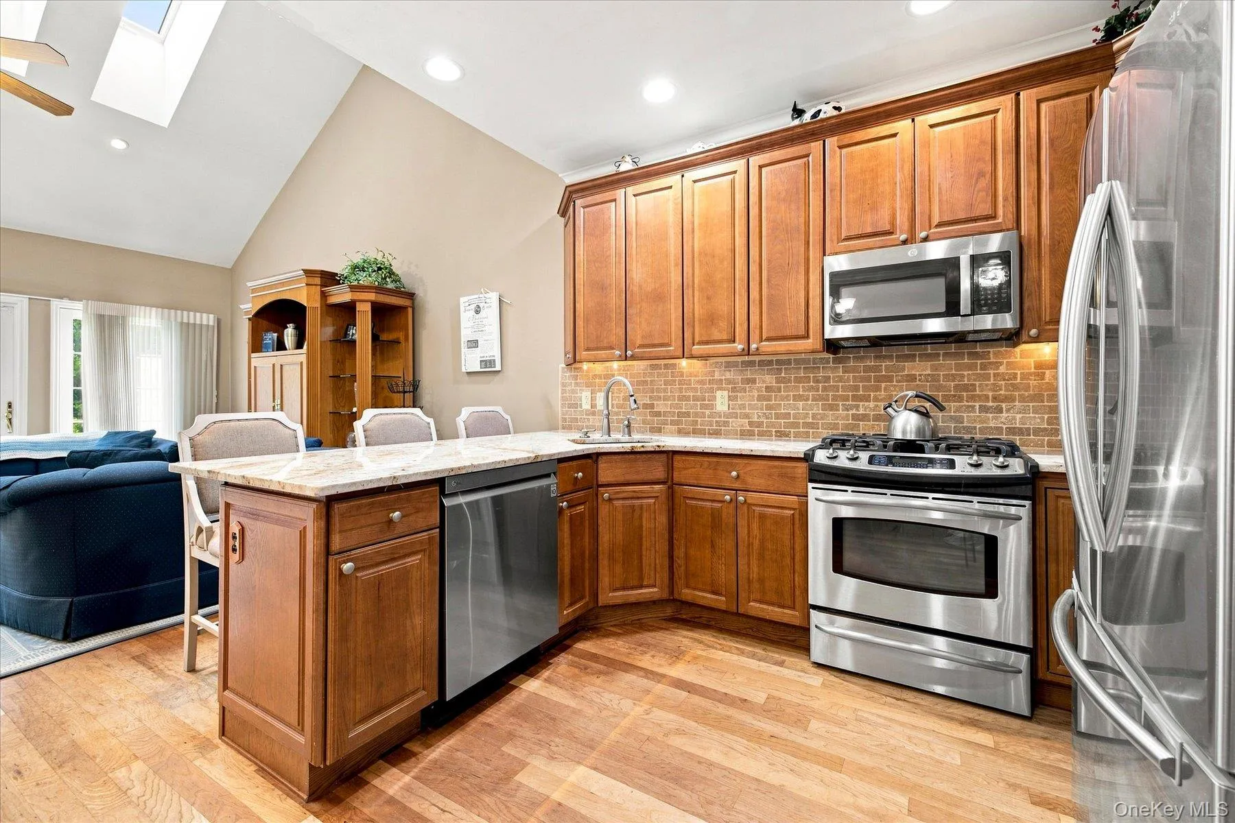 Kitchen featuring wood-finish flooring, wood cabinetry, stainless steel appliances, a tiled backsplash, and a breakfast bar with stone countertops Kitchen featuring wood-finish flooring, wood cabinetry, stainless steel appliances, a tiled backsplash, and a breakfast bar with stone countertops